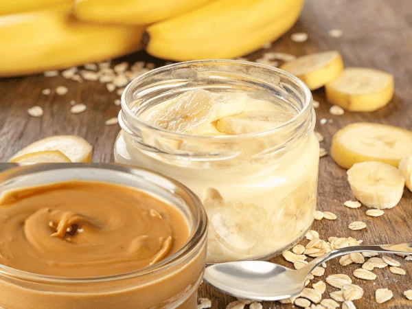 A bowl of mashed bananas next to a jar of peanut butter, the two main ingredients used for the frozen peanut butter and banana homemade dog treats recipe