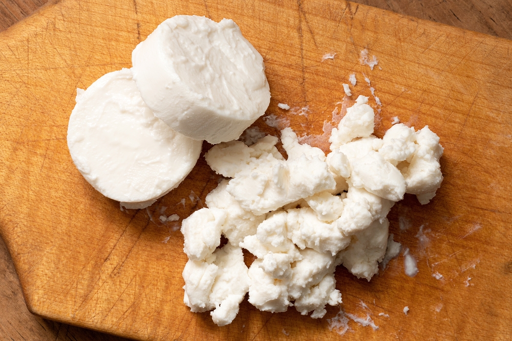 Two rounds of goat cheese and crumbled goat cheese on wood chopping board