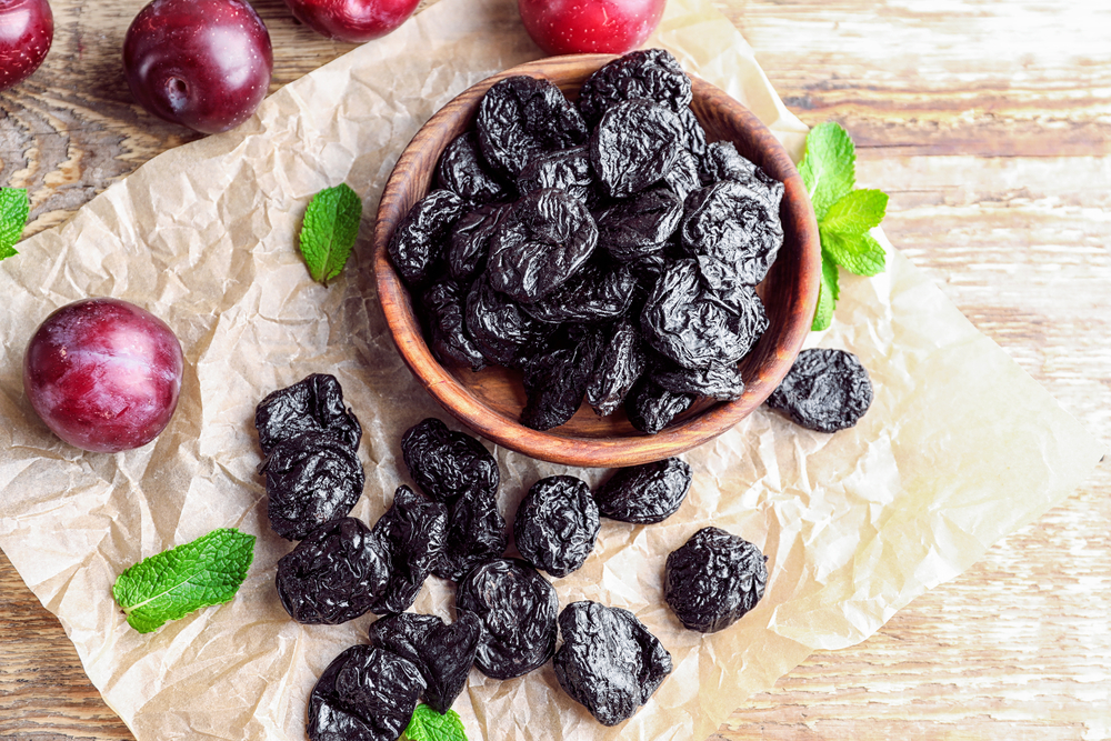 Bowl with tasty dried plums on table